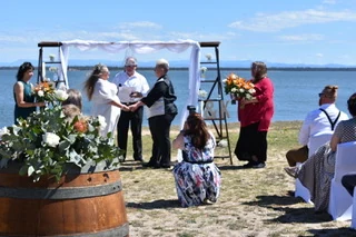 A bayside ceremony under a ladder arch, with flowers in a wine barrel