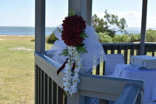 Red and white flowers tied to a gazebo rail, with a bay behind