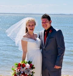 A bride and groom smiling at the water’s edge, her veil lifting in the breeze