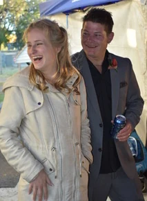 A bride in a cream coat laughing beside her groom