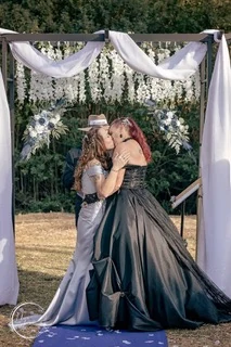Two brides kissing under a draped arch hung with white flowers