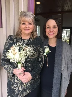 A smiling bride holding a cream bouquet beside a friend