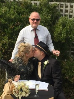 A couple kissing at the signing table as Kelvin smiles behind them