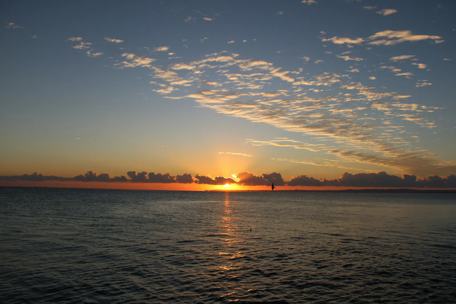 The sun setting over a calm bay under scattered cloud
